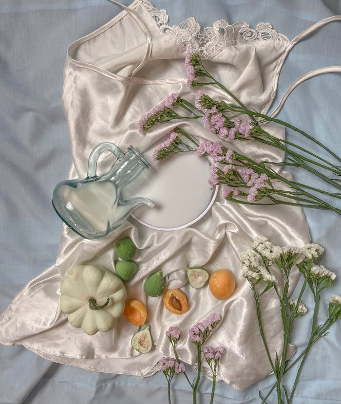 Home From above composition of silk cloth with with fruits and pumpkin placed near glass jug with wildflowers on gray textile