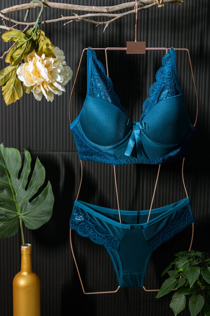 why-choose-us Blue lingerie set on hanger with decorative leaves and flowers against dark background.