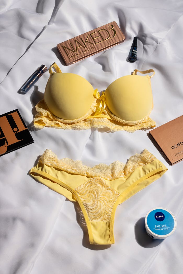Home Flat lay of yellow lingerie set with beauty products on a white background.